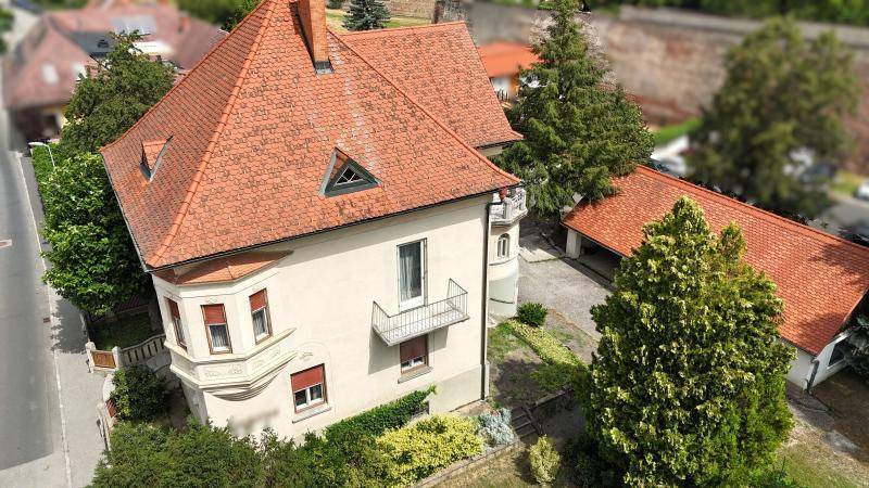 Historische Villa mit rotem Ziegeldach, Balkon und gepflegtem Vorgarten.