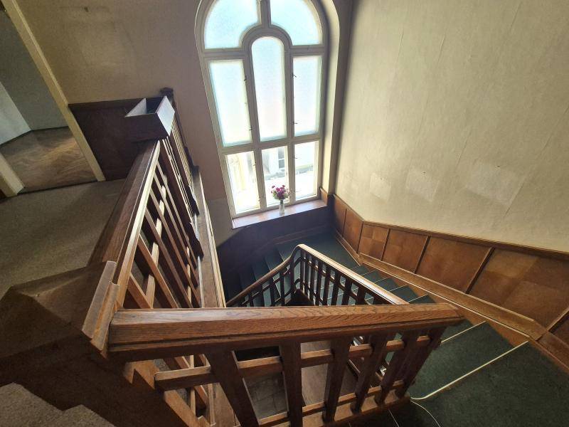 Elegantes Treppenhaus mit Holzvertäfelung, Teppichstufen und einem hohen Bogenfenster.