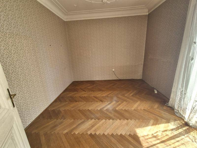 Helles Zimmer mit Fischgrätparkett, gemusterter Tapete und Stuckdecke.