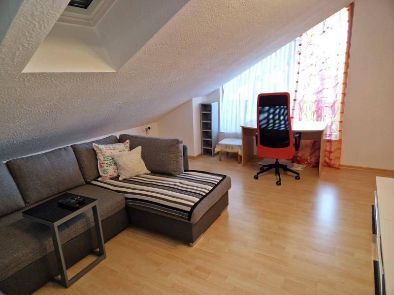 Helles Zimmer im Dachgeschoss mit Sofa, Schreibtisch und Dachschräge.