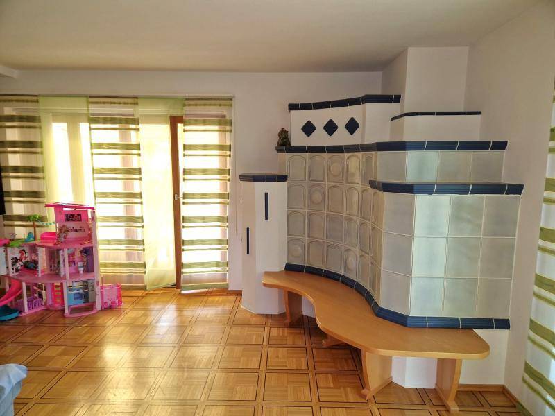 Helles Wohnzimmer mit Parkettboden, Kachelofen und Zugang zur Terrasse.