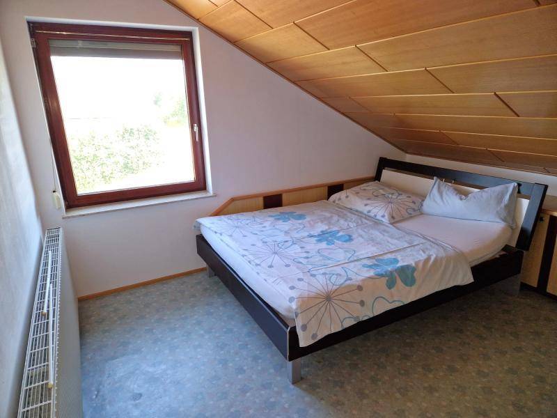 Schlafzimmer im Dachgeschoss mit Doppelbett, Holzdecke und Fenster.