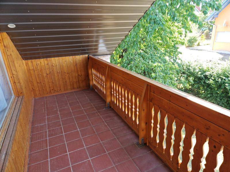 Überdachter Balkon mit Holzgeländer, Fliesenboden und Blick ins Grüne.