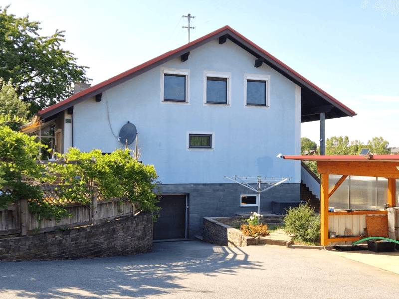 Vorderansicht des Hauses mit hellblauer Fassade, Garagenzugang und gepflasterter Einfahrt.