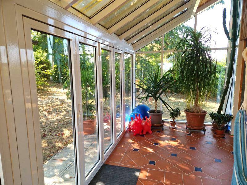 Heller Wintergarten mit Terracotta-Fliesen, vielen Pflanzen und Blick in den Garten.