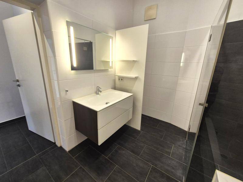 Badezimmer mit modernem Waschtisch, beleuchtetem Spiegel und dunklen Bodenfliesen.