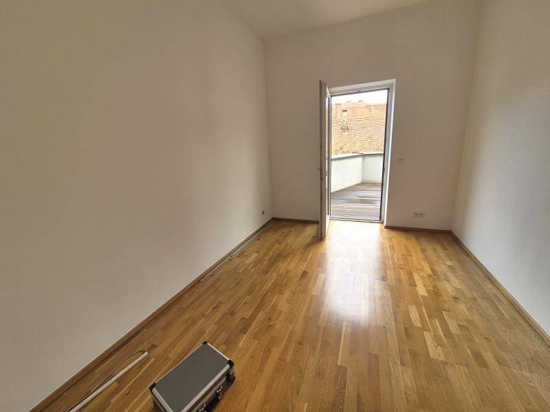 Heller Raum mit Holzboden, weißen Wänden und Zugang zu einer Außenterrasse.