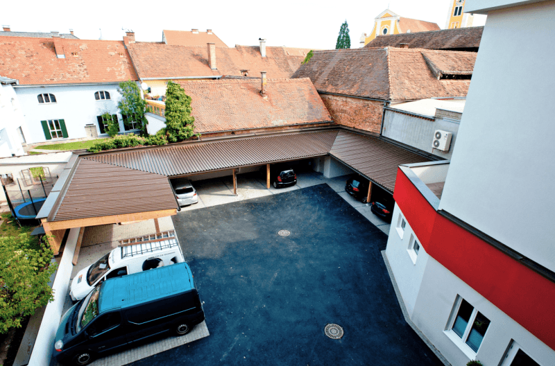 Innenhof mit mehreren überdachten Stellplätzen und geparkten Fahrzeugen, umgeben von historischen Gebäuden.