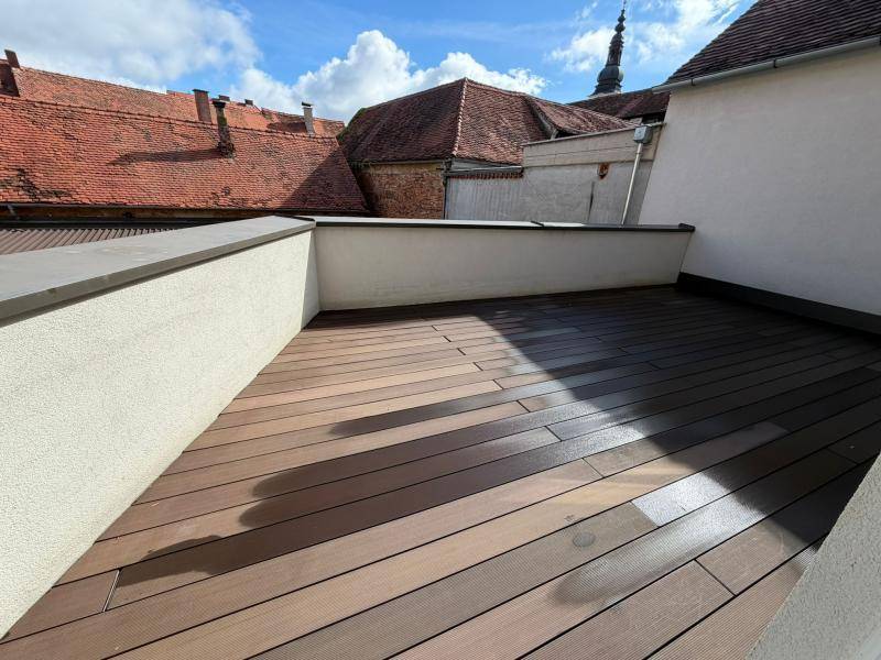 Geräumige Terrasse mit dunklem Holzdeck und Blick auf die historischen Dächer der Umgebung.