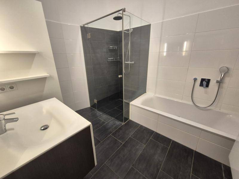 Helles Badezimmer mit dunklen Fliesen, Badewanne, begehbarer Dusche und modernem Waschtisch.