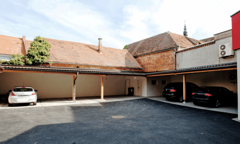 Innenhof mit überdachten Parkplätzen und geparkten Autos, umgeben von traditionellen Gebäuden.