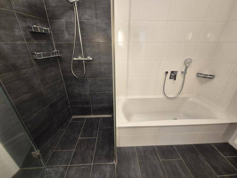 Badezimmer mit dunklen Bodenfliesen, weißen Wandfliesen, Badewanne und einer geräumigen begehbaren Dusche.