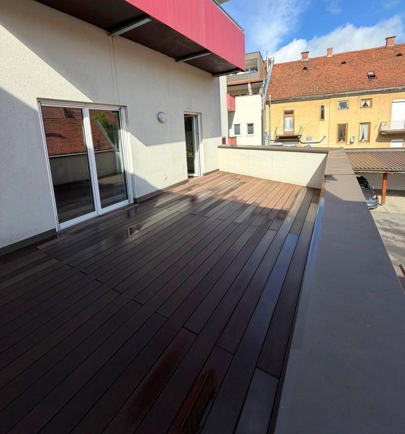 Große Terrasse mit Holzdeck und zwei Zugängen zum Gebäude, bietet Blick auf die Nachbarschaft.