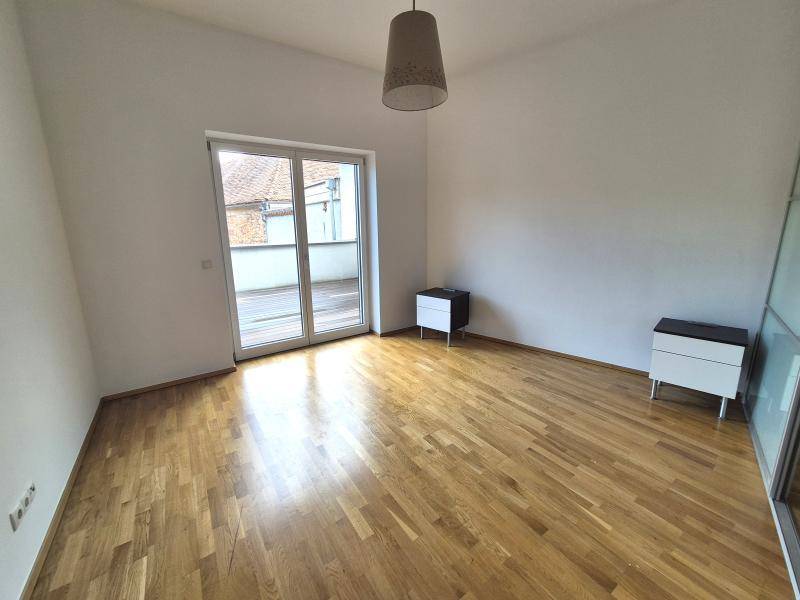 Schlafzimmer mit Holzboden, weißen Wänden und direktem Zugang zu einer Terrasse durch eine große Glasschiebetür.