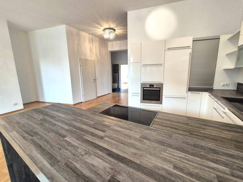 Moderne Einbauküche mit weißen Hochglanzfronten, integriertem Backofen und Kochinsel mit Induktionskochfeld.