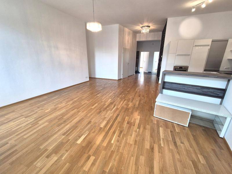 Geräumiger offener Wohnbereich mit Holzboden, weißen Wänden und Blick zur Küche und zum Flur.