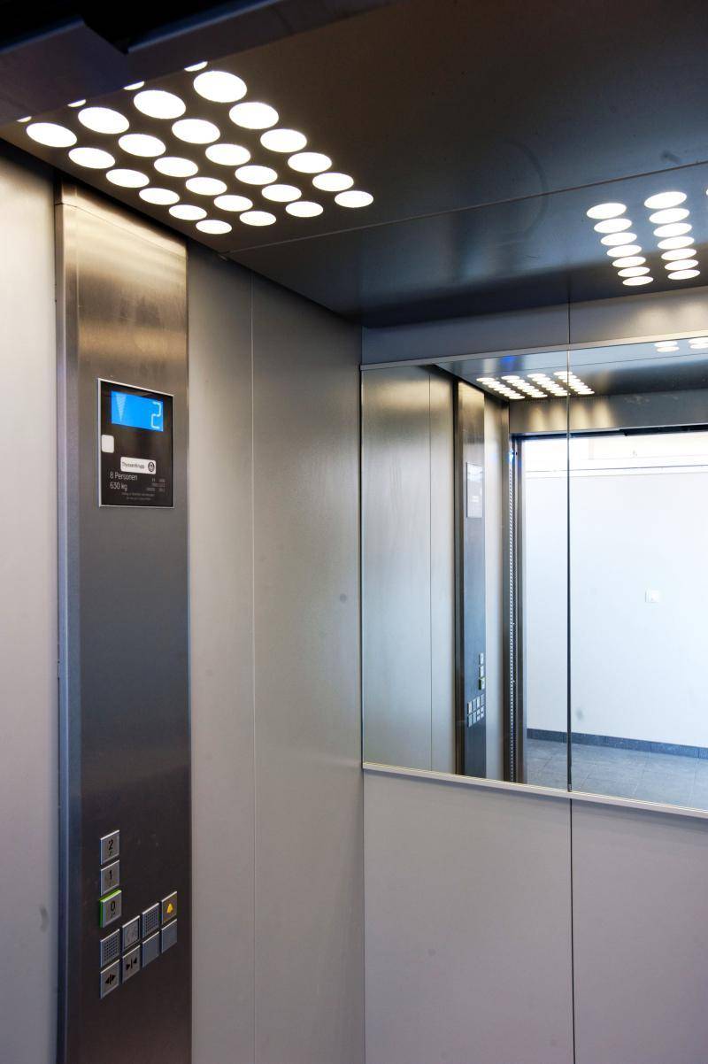 Innenansicht eines modernen Aufzugs mit Edelstahlverkleidung, Spiegel und beleuchteter Decke.