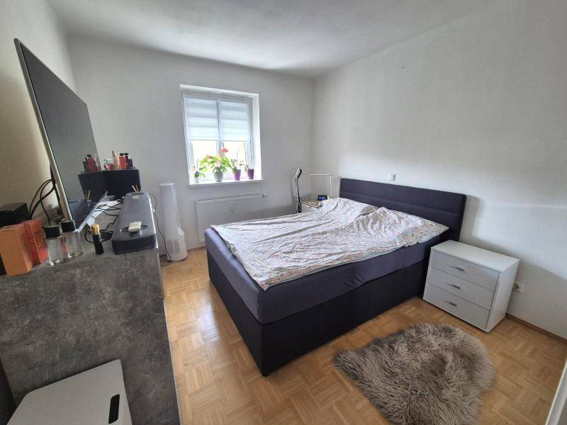 Helles Schlafzimmer mit Doppelbett, Parkettboden und einem Fenster für natürliches Licht.