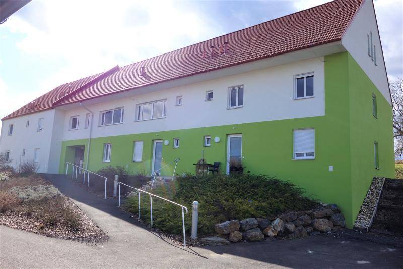 Modernes Mehrfamilienhaus mit grüner Fassade und barrierefreiem Zugang über eine Rampe.
