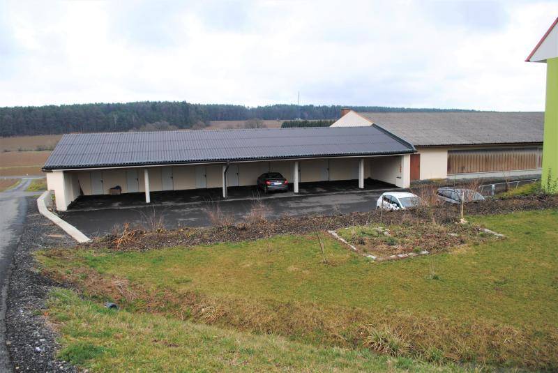 Außenbereich mit Carport-Parkplätzen und einer kleinen Gartenfläche im Vordergrund.