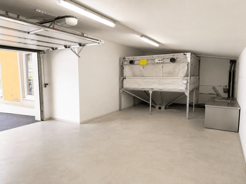 Helle Garage mit Betonboden, offenem Tor und industrieller Ausstattung.
