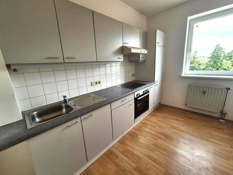 Funktionale Küche mit grauen Schränken, weißem Fliesenspiegel und Fenster mit Ausblick ins Grüne.