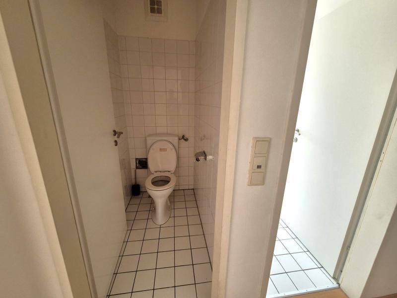 Separates WC mit weißen Fliesen und Toilette, zugänglich über einen schmalen Flur.