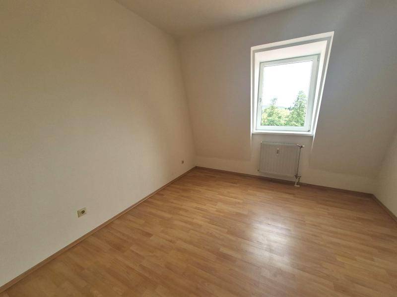 Weiteres helles Zimmer mit Dachschräge, Laminatboden und Fenster mit Ausblick ins Grüne.