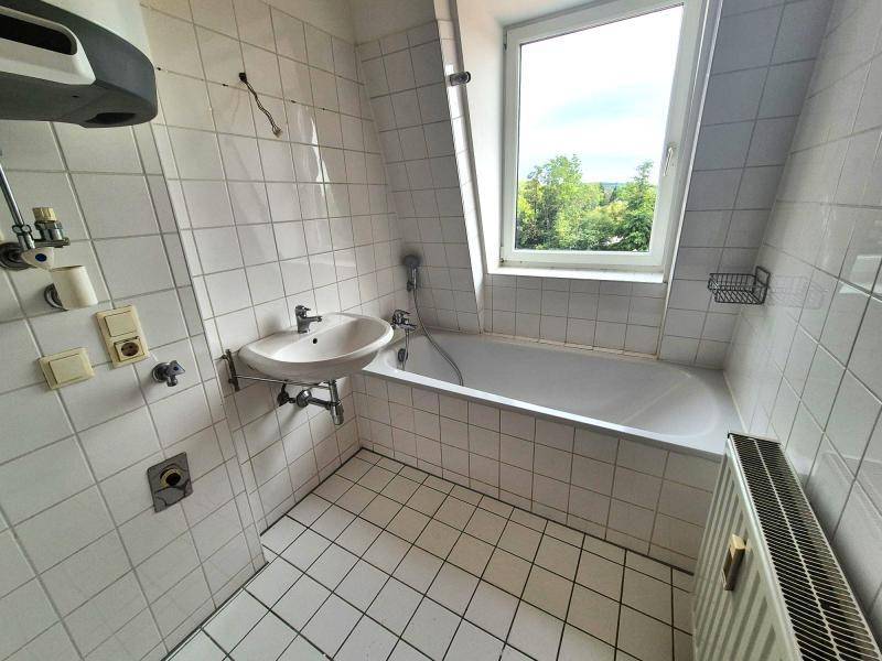 Badezimmer mit weißen Fliesen, Badewanne, Waschbecken und Fenster mit Blick ins Grüne.