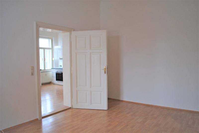 Heller Raum mit Holztür, die den Blick in die angrenzende, modern ausgestattete Küche freigibt.