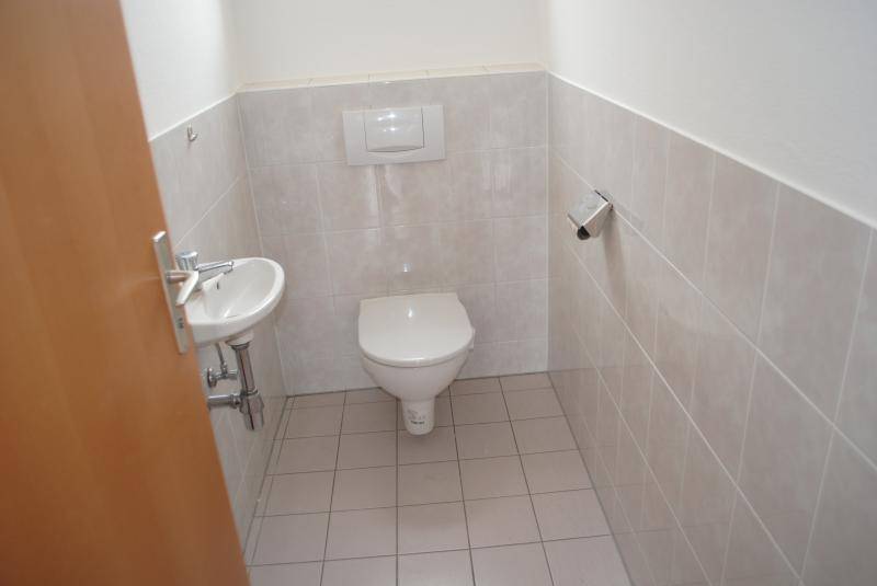 Separates Gäste-WC mit wandhängender Toilette, kleinem Waschbecken und hellen Fliesen.