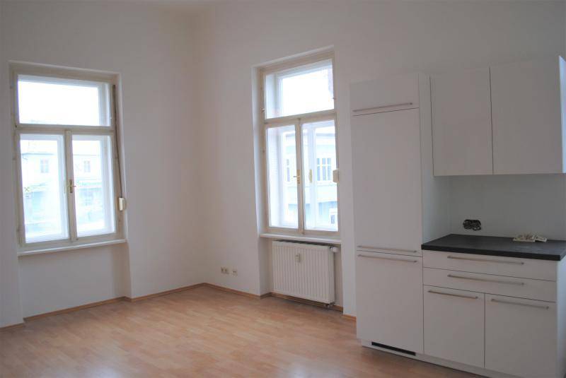 Geräumige Küche mit zwei großen Fenstern, weißen Einbauschränken und hellem Laminatboden.