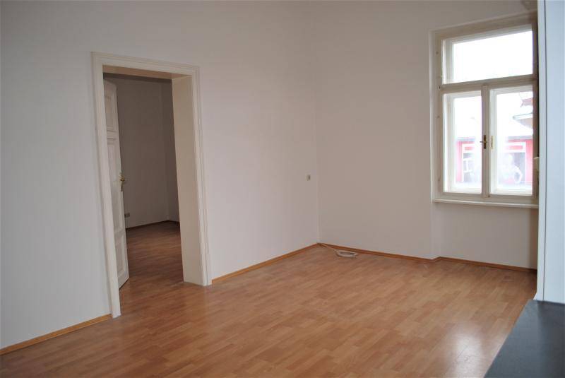 Heller, leerer Raum mit Fenster und offener Tür, die zu einem weiteren Zimmer führt.