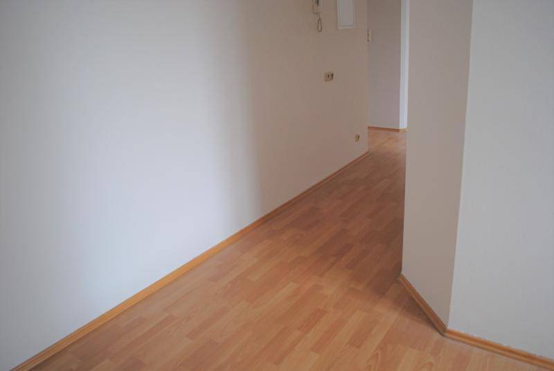 Langer, heller Flur mit Laminatboden und weißen Wänden, der verschiedene Räume verbindet.