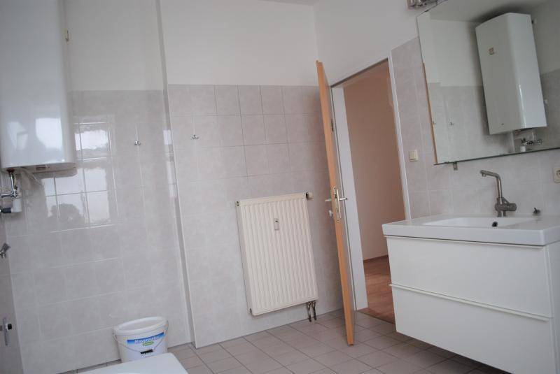 Badezimmer mit Waschbeckenunterschrank, Spiegel, Heizkörper und hellen Fliesen an Wänden und Boden.