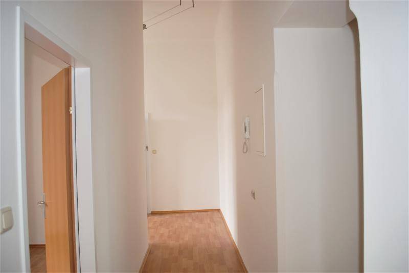 Heller Flur mit offener Tür und Blick in den hinteren Bereich, ausgestattet mit Laminatboden.