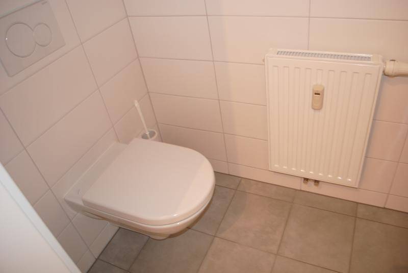 Separates WC mit wandhängender Toilette, Heizkörper und hellen Fliesen.