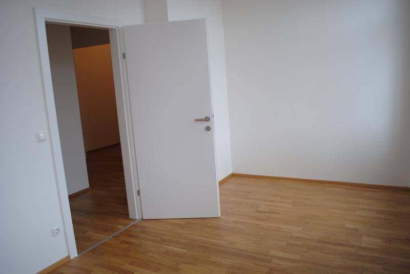 Innenraum mit heller Holzboden und offener Tür, die den Blick in einen weiteren Raum freigibt.