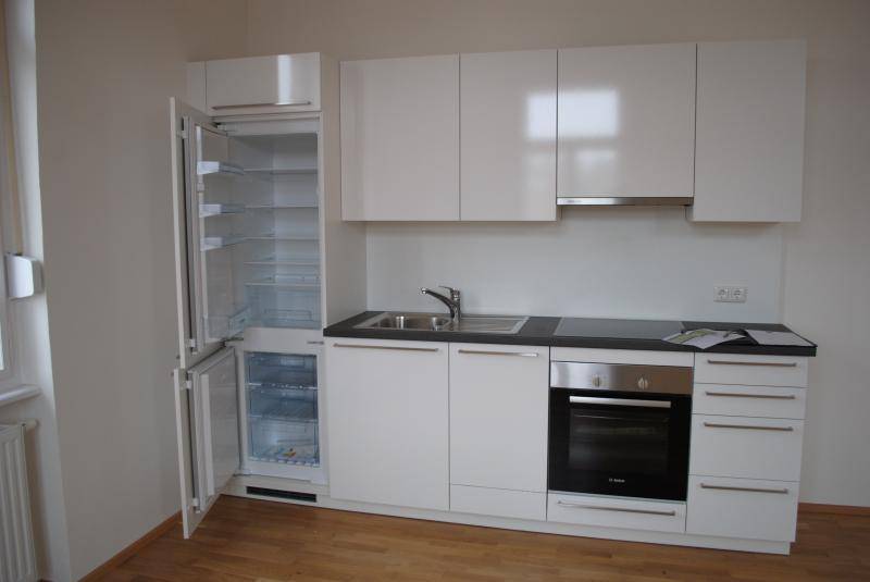 Moderne Küchenzeile mit integrierten Geräten, Backofen und Kühlschrank in Hochglanzweiß.
