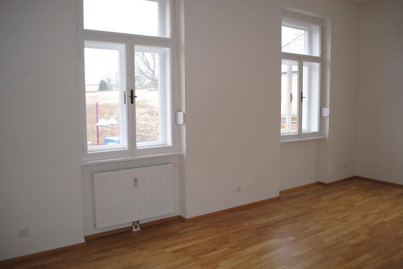 Geräumiger, leerer Wohnraum mit großen Fenstern und hellem Parkettboden.