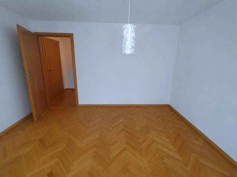 Leeres Zimmer mit Fischgrätparkettboden, weißen Wänden und einer Holztür, bereit zur individuellen Gestaltung.