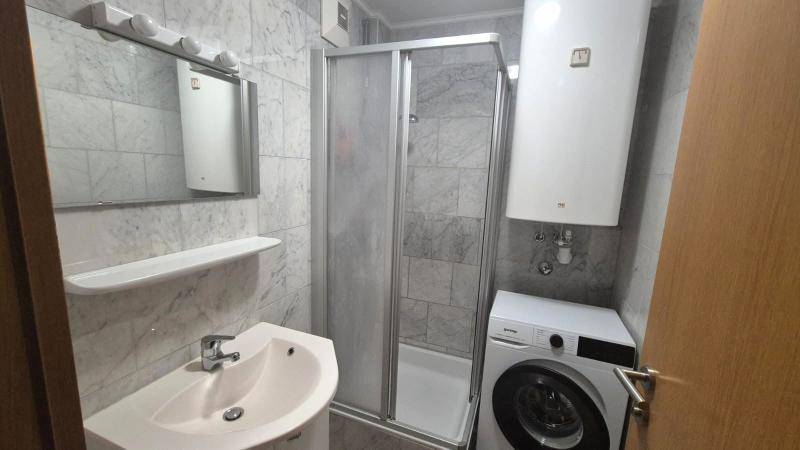 Modernes Badezimmer mit Duschkabine, Waschbecken, Spiegel und Waschmaschine, komplett gefliest.