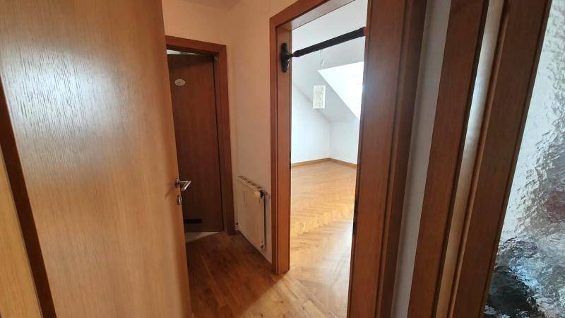 Flur mit Holztüren und Blick in ein helles Zimmer mit schrägen Wänden und Parkettboden.