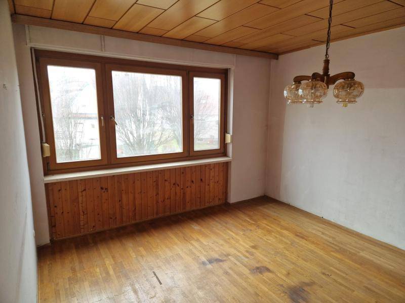 Leerer Raum mit Holzboden, Holzdecke und großem Fenster, das Tageslicht hereinlässt.
