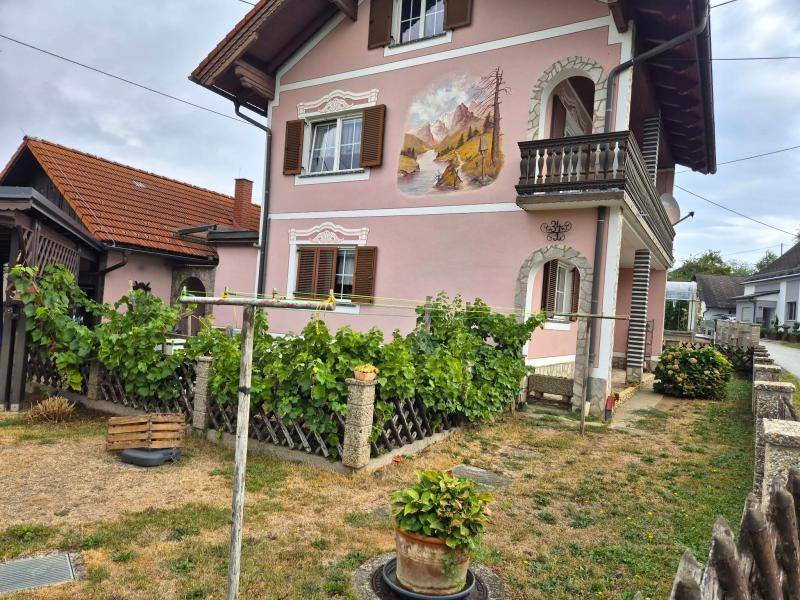 Rosafarbenes Haus mit traditionellen Fensterläden, Balkon und einem trockenen Vorgarten mit Wäscheleine.