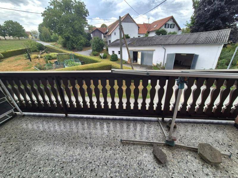 Blick vom Balkon auf die ländliche Umgebung mit weiteren Häusern und viel Grün.