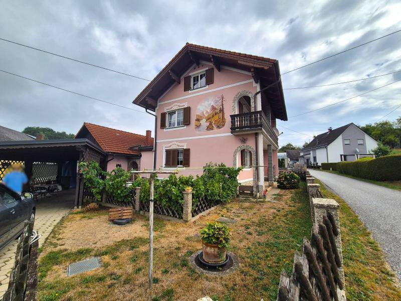 Ansicht des Hauses mit rosafarbener Fassade, Carport und einem trockenen Rasenbereich im Vorgarten.