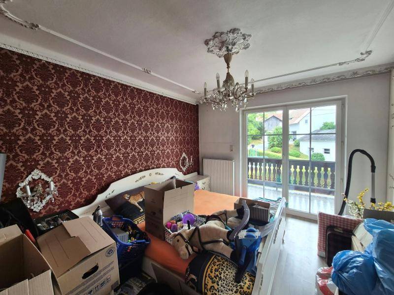 Schlafzimmer mit auffälliger roter Tapete, Stuckdecke und Zugang zum Balkon, derzeit unaufgeräumt.