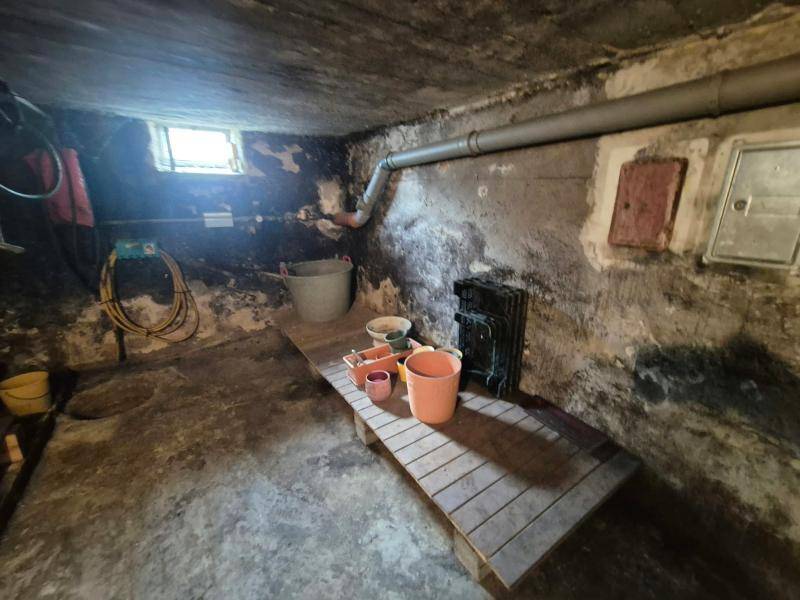 Unausgebauter Kellerraum mit sichtbaren Rohren, kleinem Fenster und einfacher Holzablage.