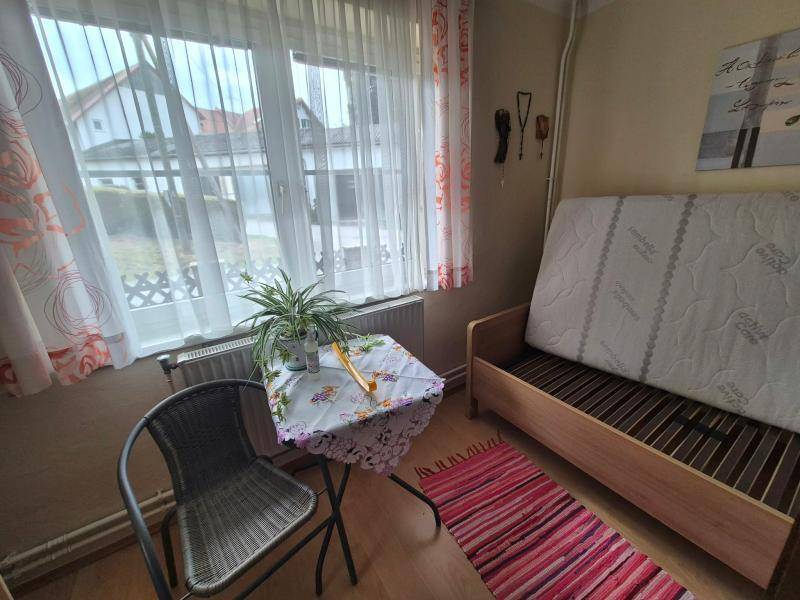 Helles Zimmer mit großem Fenster, Laminatboden und einfacher Einrichtung, ideal als Gästezimmer.